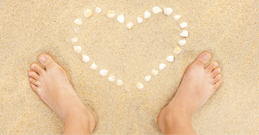 Shells formed into heart on beach sand with feet pointing to the outer edge